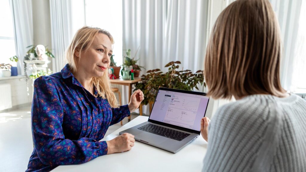 Viestinnän asiantuntija Anu Dufva sparraa asiakasta. Heidän välissään olevan tietokoneen ruudulla näkyy somekanavan tilastoja.